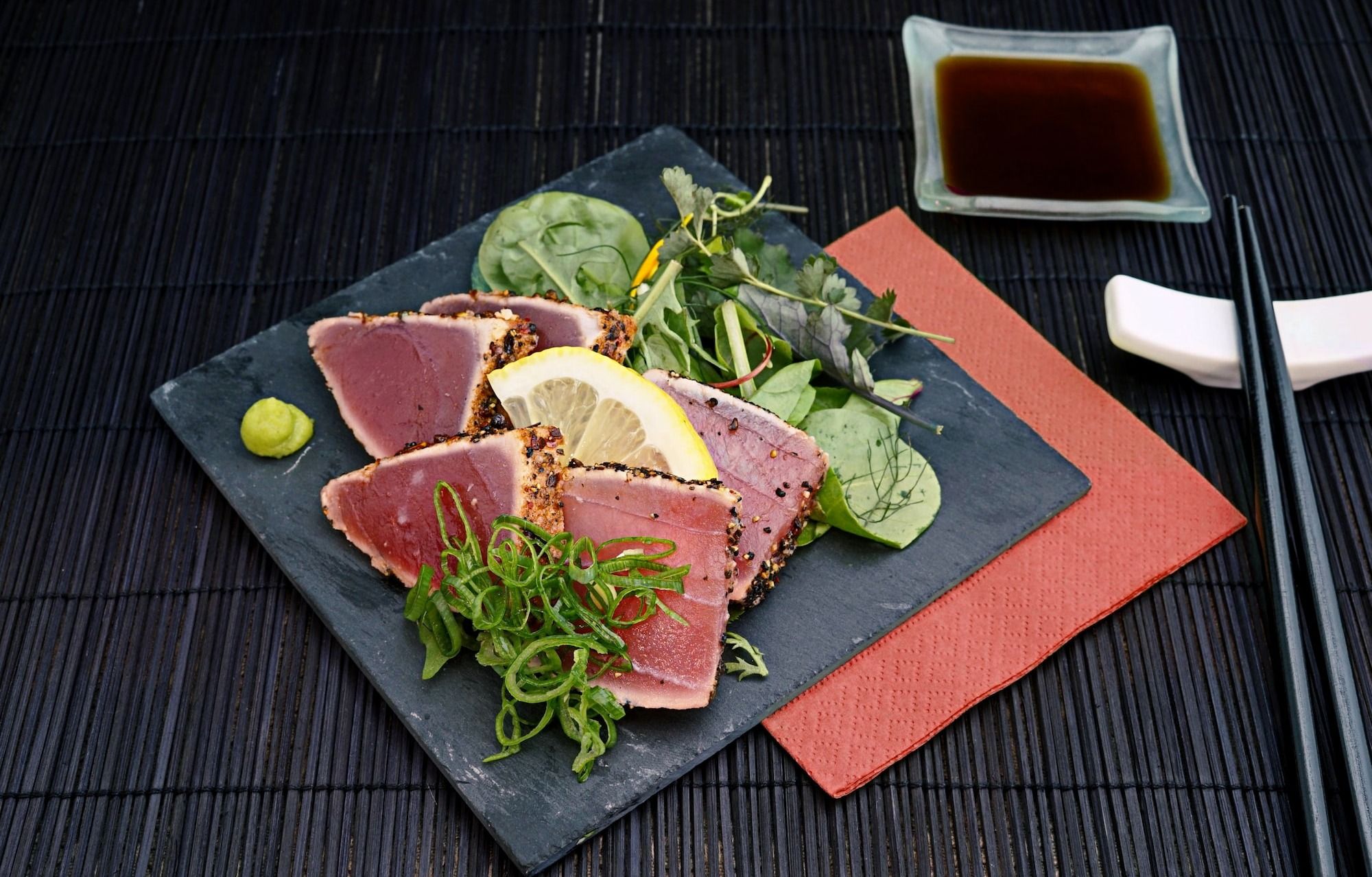 tuna with lemon and greens salad on black plate